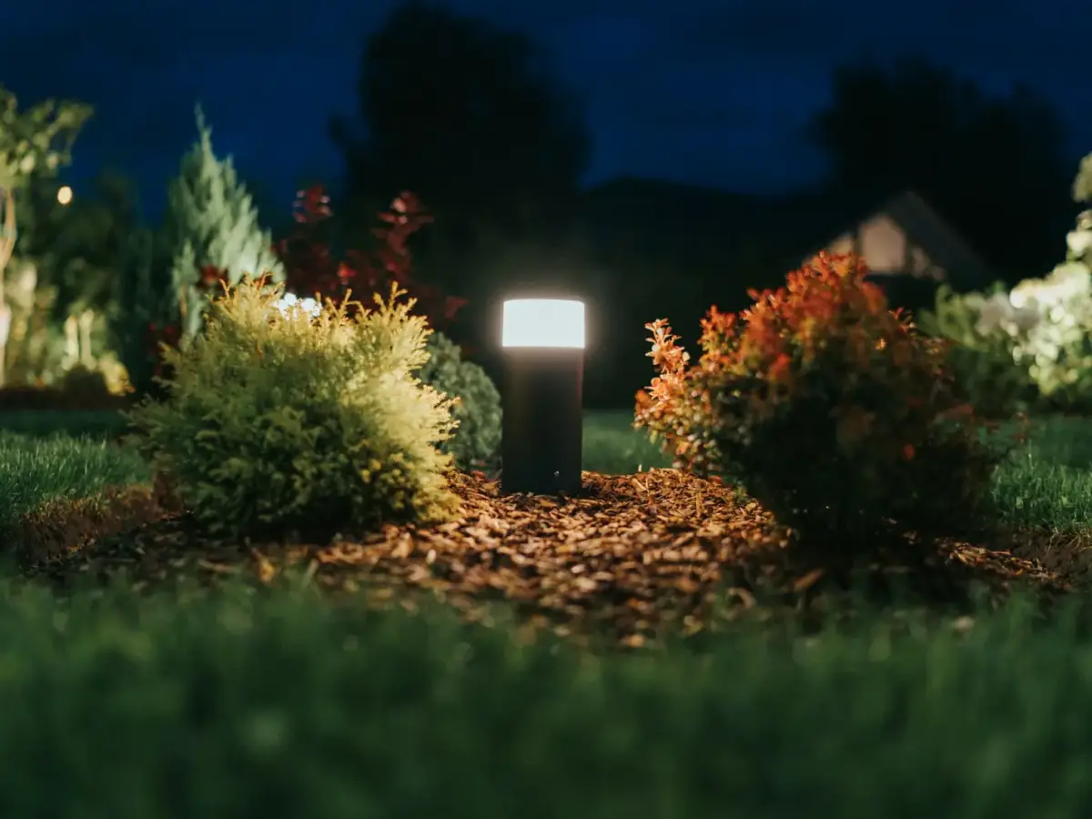 Pollerleuchte, die bei Nacht Sträucher in einem Garten beleuchtet