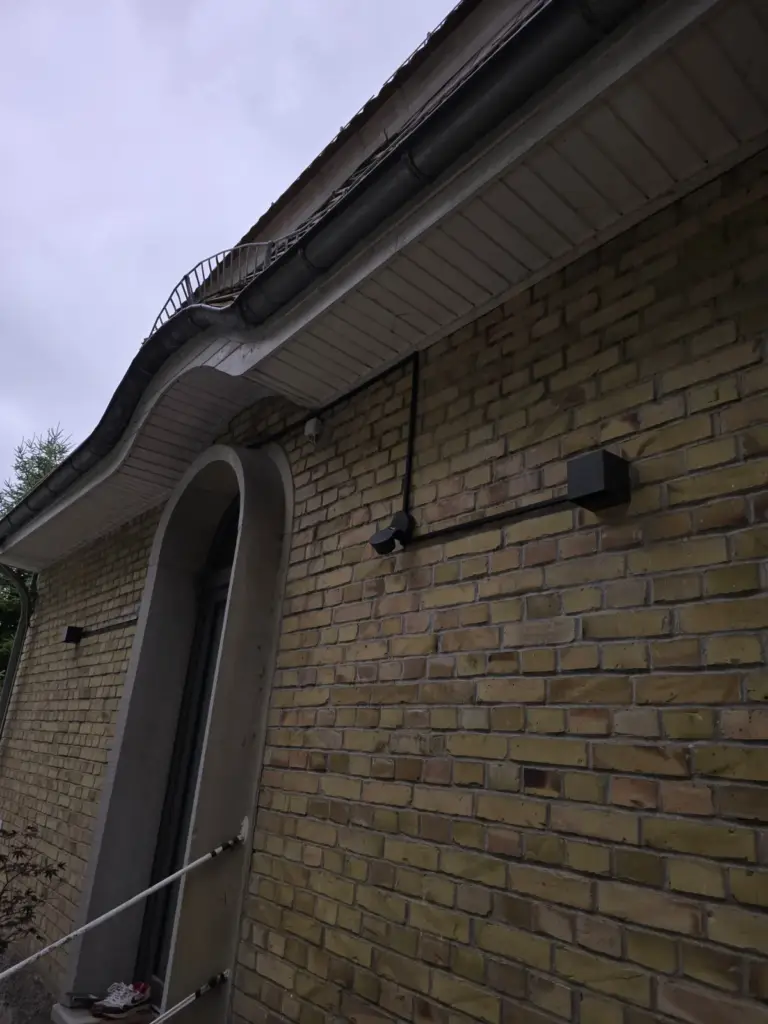 Außen an einer Klinkerfassade verlegte Leitung mit Anschlussdose unter dem Dachüberstand
