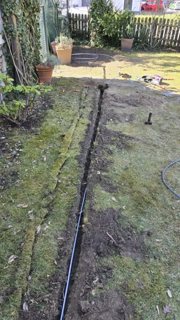 Offener Graben in einem Garten mit frisch verlegter Leitung